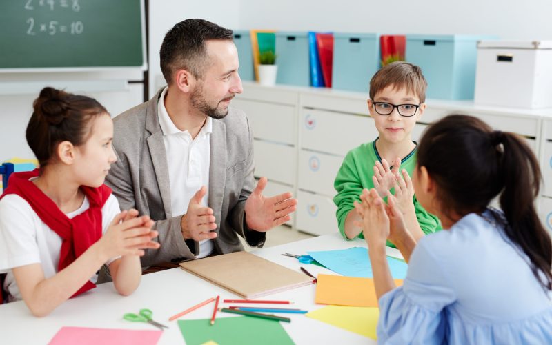 Group of cute schoolkids and their teacher discussing size of something at lesson