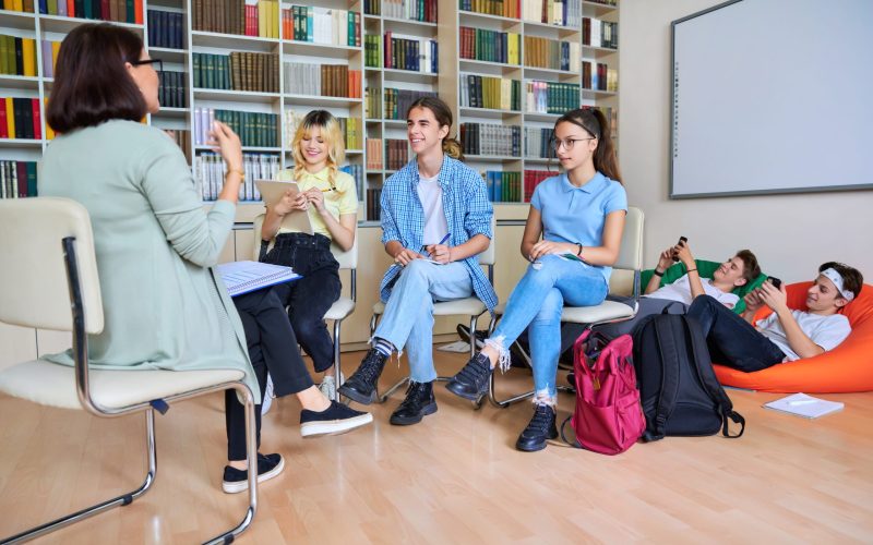 Female mentor teacher working with male teenage high school students in the library. Education, knowledge, adolescence, consultation, support, school, college concept