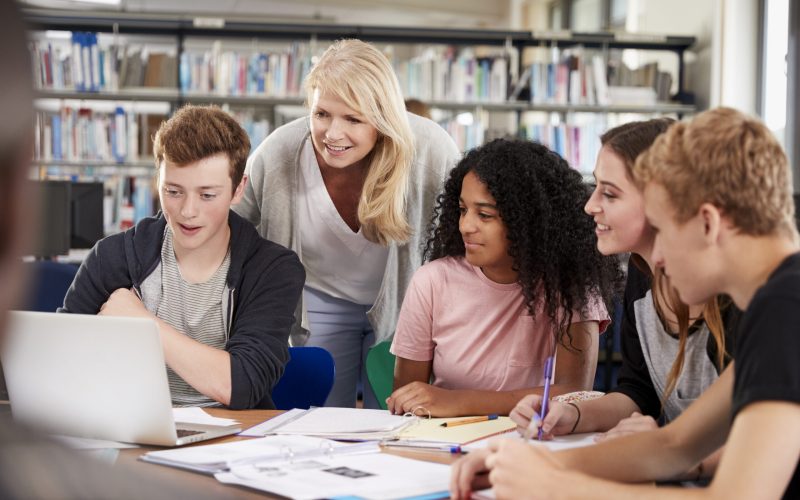 Female Teacher Working With College Students In Library