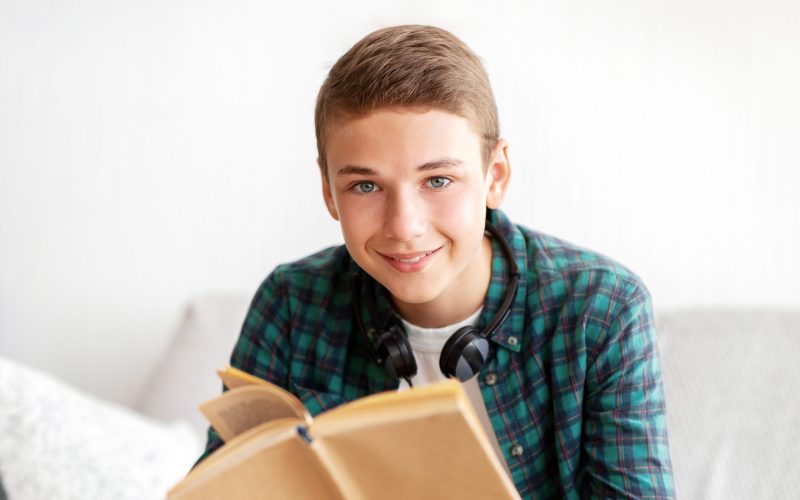 Happy teenager enjoying his book, spending time at home alone, copy space